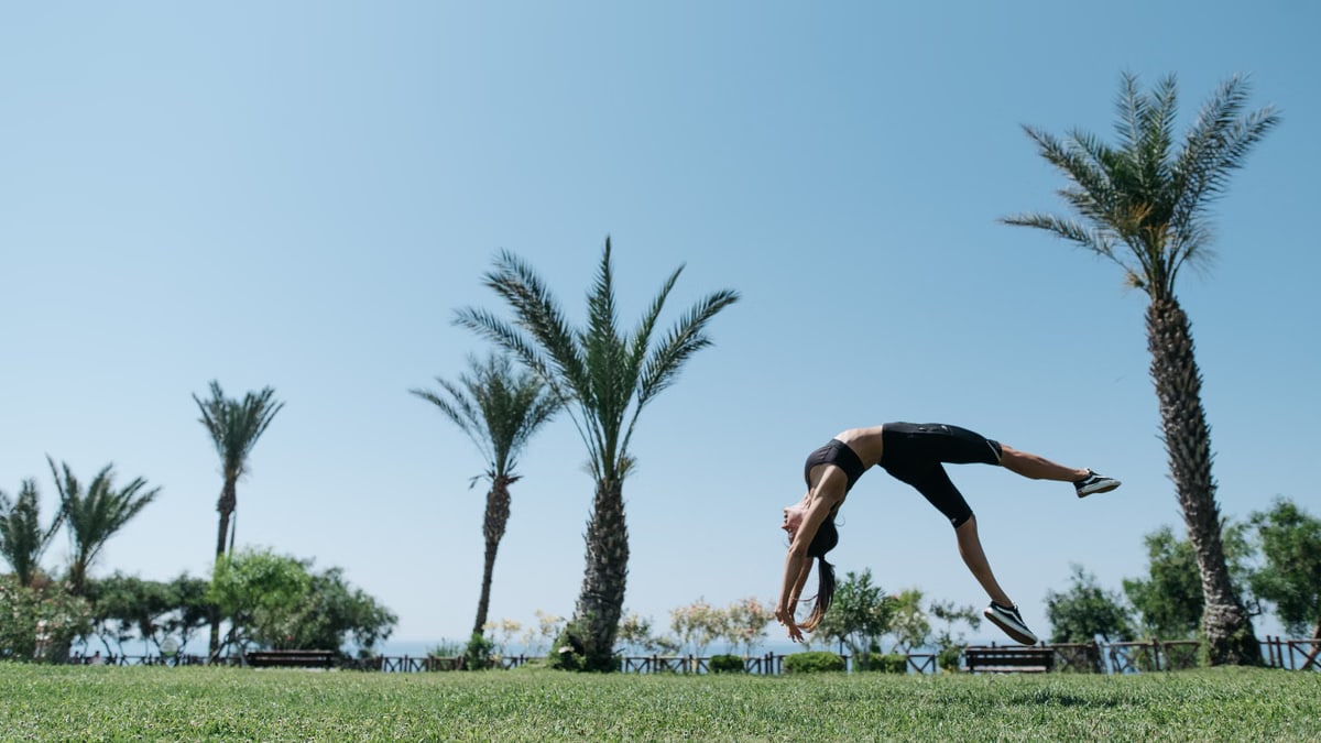 Athletic woman executing a backflip amidst palm trees in a sunny outdoor park.